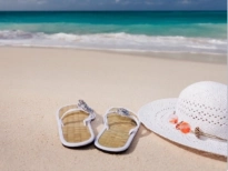 A pair of flip-flops and a sun hat sitting on a sandy beach with ocean waves in the background